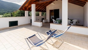 A covered outdoor patio with a wooden ceiling, white walls, and a view of a mountain. There are two blue and white chairs and a table with white chairs. - Cosy apartment for 4 people with WIFI, balcony, pets allowed and panoramic view (Andora)