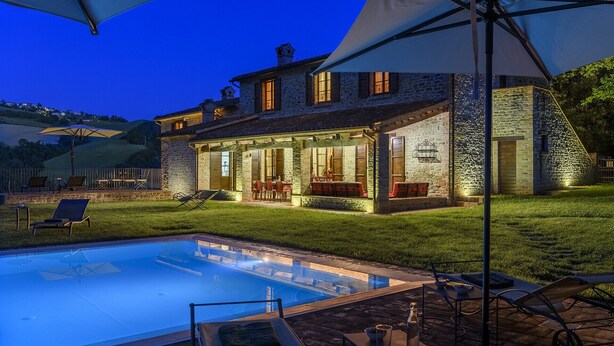 Una casa de piedra con piscina, mobiliario exterior y un patio cubierto.
