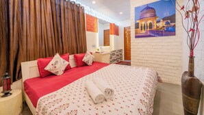 Quarto de hotel com cama, mesa de cabeceira, abajur, quadro na parede e um vaso decorativo.