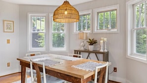 A dining area with a wooden table, white chairs, a hanging rattan light fixture, and large windows with a view of greenery. - Peaceful 2/2 with VIEWS: Echota (Banner Elk)