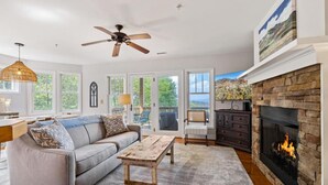 A spacious living room with a fireplace, a ceiling fan, and a large window overlooking a deck. - Peaceful 2/2 with VIEWS: Echota (Banner Elk)