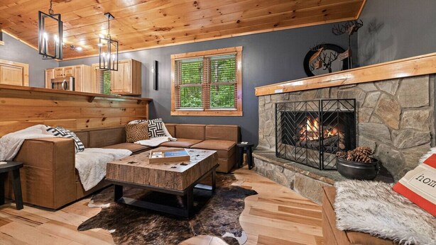 A cozy cabin interior with a stone fireplace, wooden ceiling, and a seating area with a coffee table.