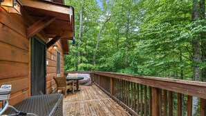 A wooden deck with a table and chairs, surrounded by a wooden railing, overlooking a forested area.