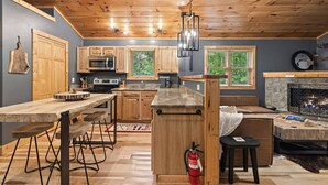 A modern kitchen with wooden cabinets, a large island, and a stone fireplace.