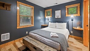 A bedroom with a large bed, wooden headboard, two bedside tables with lamps, a ceiling fan, and a window with blinds.