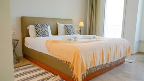 Habitación de hotel con una cama grande, una mesita de noche, una lámpara y vistas al exterior.