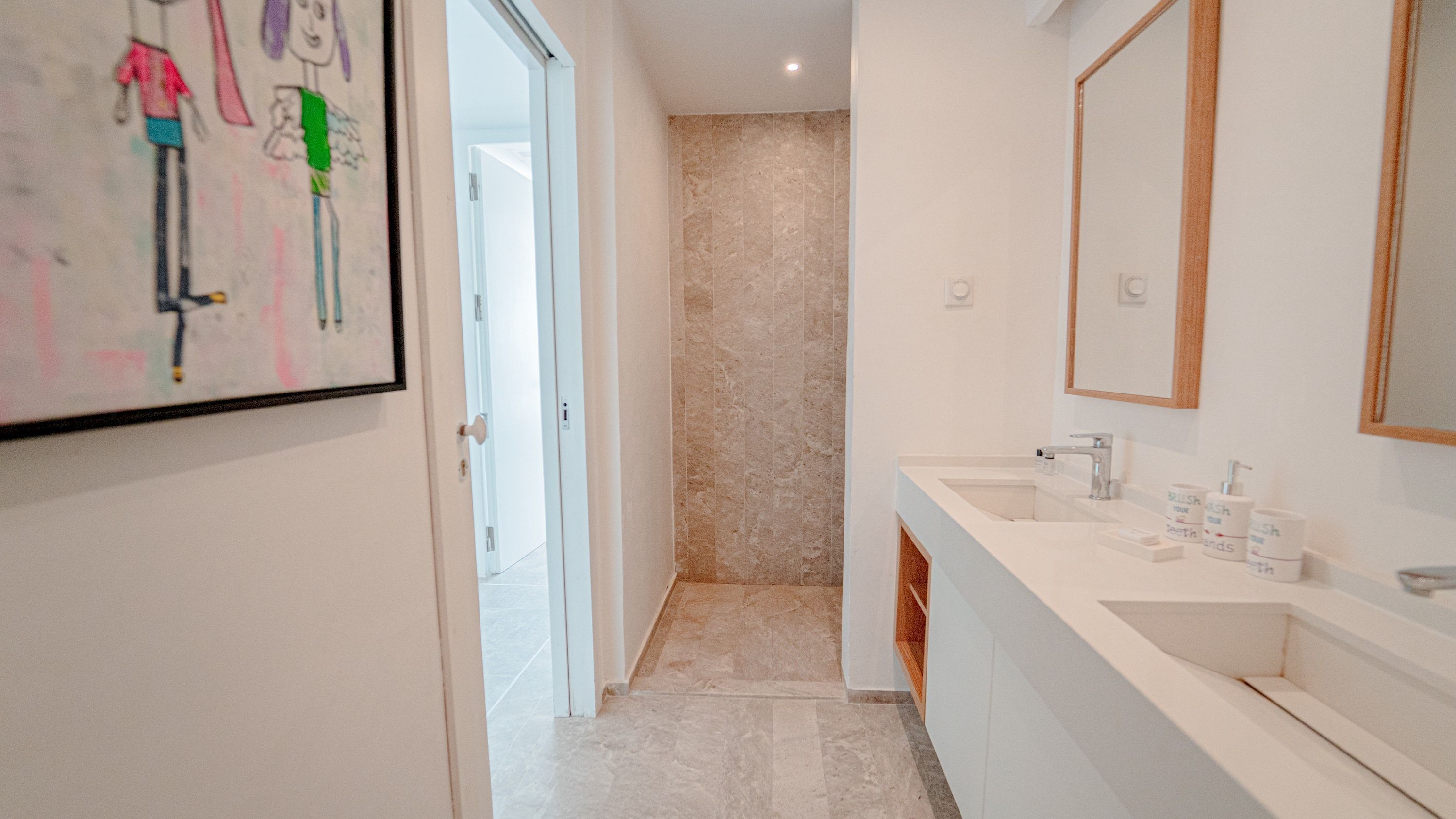 A modern bathroom with a marble wall, a large mirror, and a white sink with toiletries.