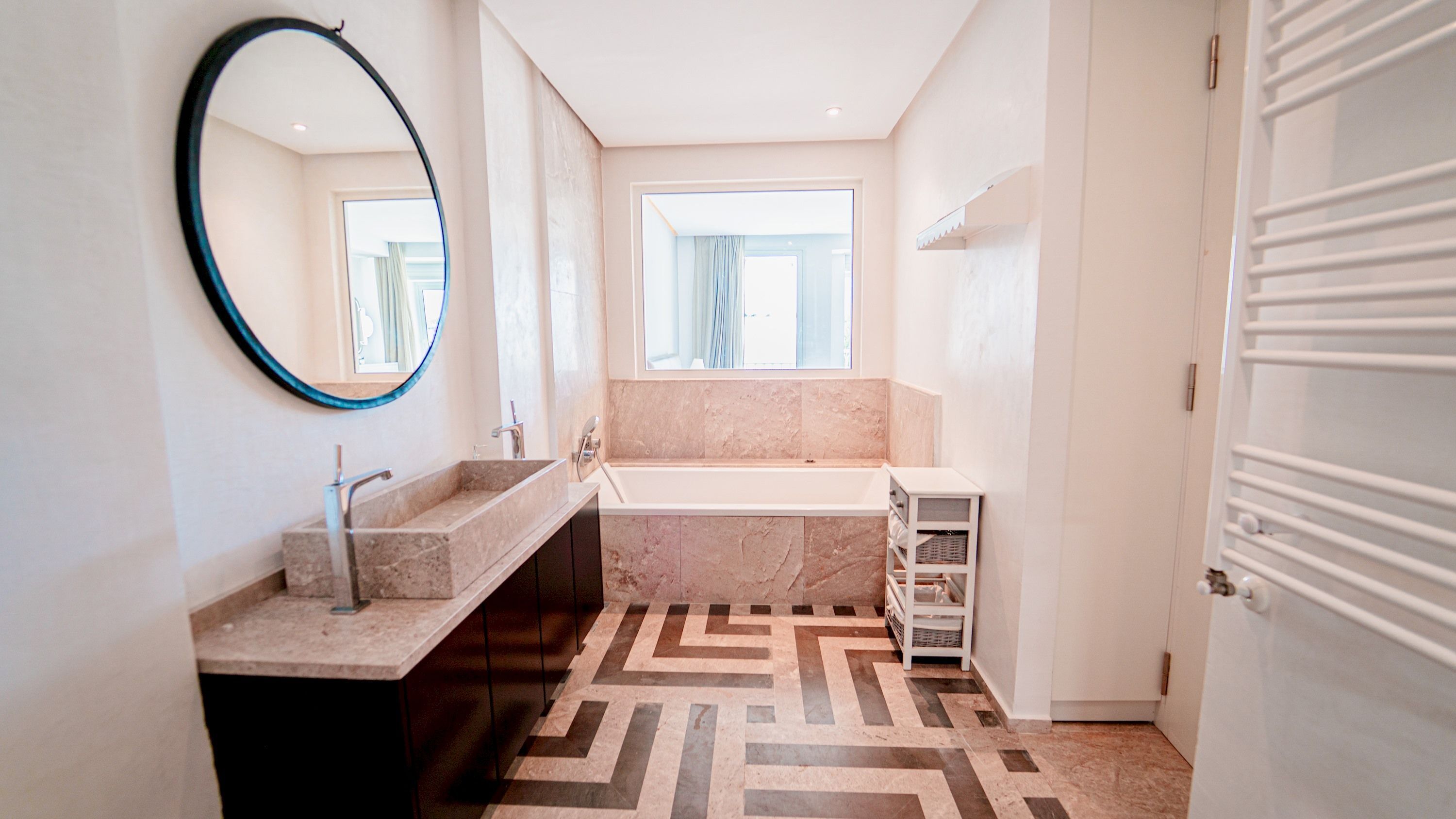 Un bagno moderno con una vasca da bagno freestanding, uno specchio grande e un pavimento decorato.