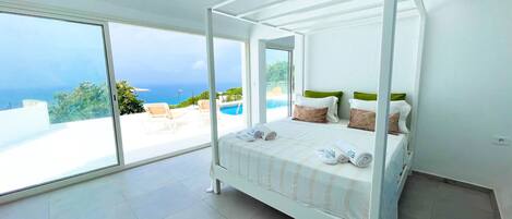 A four-poster bed with a view of the sea and a pool.