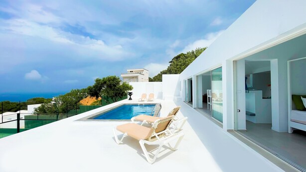 A modern outdoor pool area with lounge chairs, a clear view of the sea, and a white building with large windows. - Padel Resort Villa Romana 2bdrs (Raf Raf)