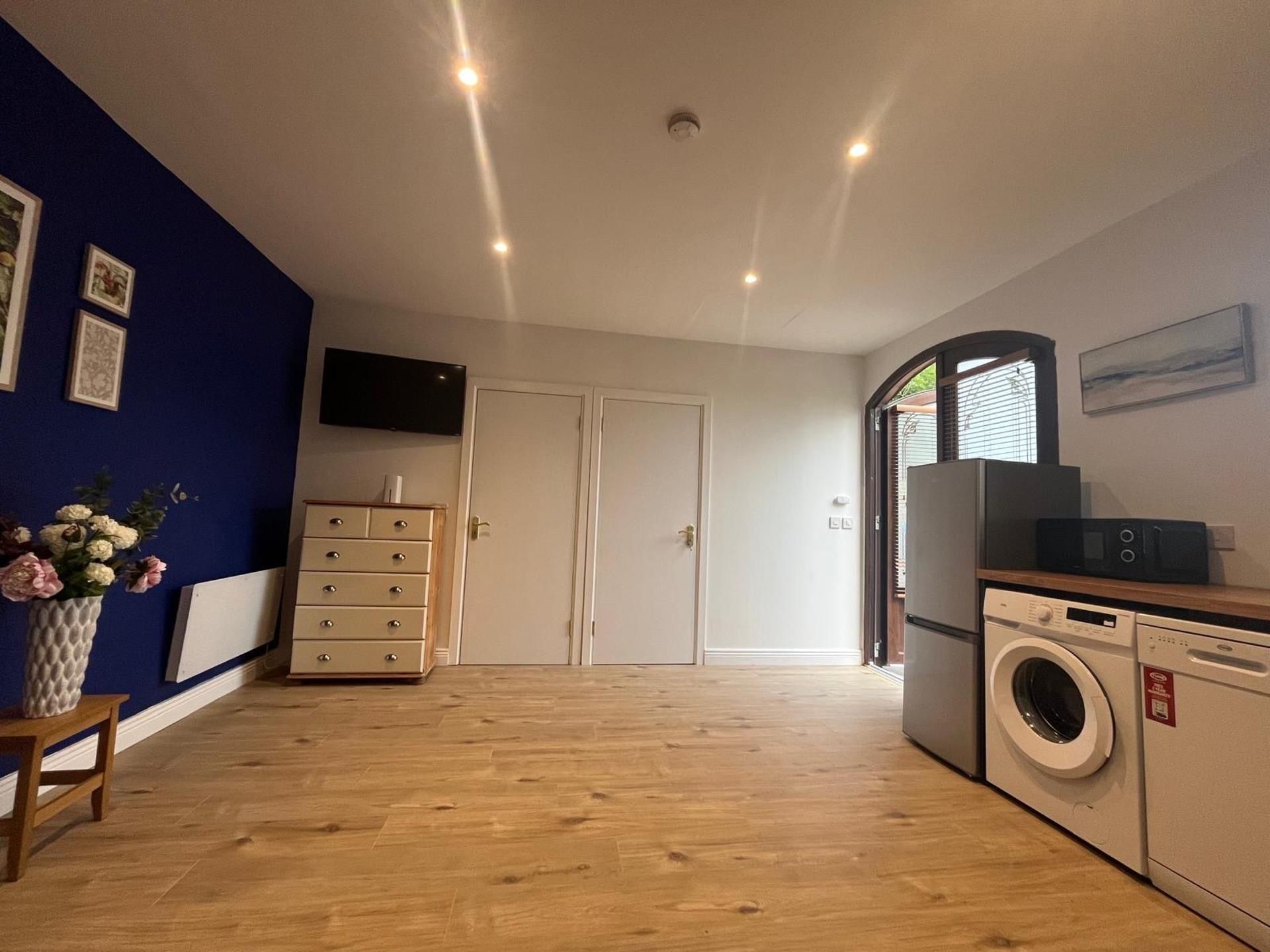 A modern kitchen with wooden flooring, a built-in washing machine, and a flat-screen TV.