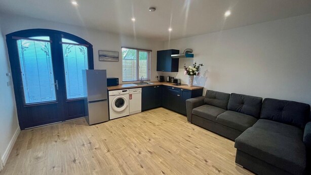 A compact living space with a kitchenette, a washing machine, a sofa, and a dining area. - 1-bed Cosy Cottage Near Emerald Park - Sleeps 5 (Rackenstown)