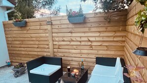 A wooden deck with two black cushioned seating areas, a small table with a candle and a bottle, and a lantern. - 1-bed Cosy Cottage Near Emerald Park - Sleeps 5 (Rackenstown)