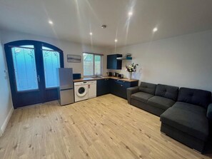 A compact living space with a kitchenette, a washing machine, a sofa, and a dining area. - 1-bed Cosy Cottage Near Emerald Park - Sleeps 5 (Rackenstown)