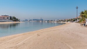 Ein Strand mit blauem Himmel, ruhiger See und Gebäuden im Hintergrund.
