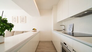 Une cuisine moderne avec des meubles blancs, un plan de travail en verre et un plancher en bois. Deux tableaux encadrés ornent le mur, et une plante en pot est posée sur le plan de travail.