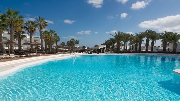 Une piscine d’eau cristalline, une plage de sable blanc et des palmiers.