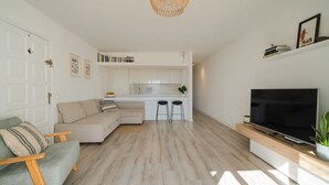 Un salon moderne avec un canapé, un téléviseur et un coin cuisine à l’arrière-plan.