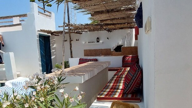 A courtyard with a tiled floor, a large pot, and a covered seating area with patterned cushions. - Welcome to Studio Jasmin in this corner of paradise in Menzel Soltane Ahmed (MIDOUN)