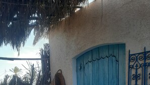 A blue door with a decorative metal gate, a white chair, and a woven basket leaning against the wall. - Welcome to Studio Jasmin in this corner of paradise in Menzel Soltane Ahmed (MIDOUN)