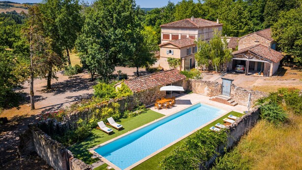 Eine Villa mit Swimmingpool, Sitzgelegenheiten im Freien und einer Steinmauer.