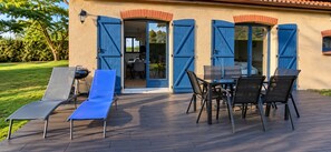 An outdoor patio with a table and chairs, a grill, and a blue door leading to an interior space.