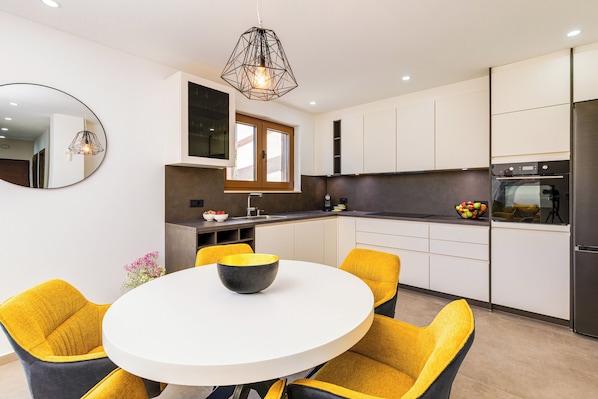 A modern kitchen with a round dining table, yellow chairs, and a large mirror on the wall.