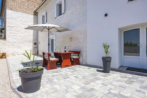An outdoor patio with a table and chairs, a large umbrella, and potted plants. - Lara Holiday Home (Kanfanar)