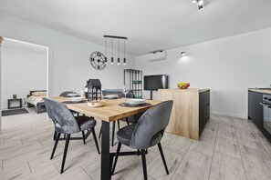 A modern dining area with a wooden table, grey chairs, a clock, and a TV. - Lara Holiday Home (Kanfanar)