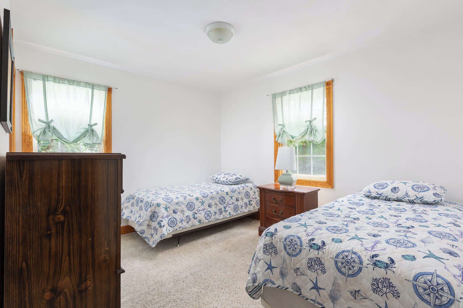 A bedroom with two single beds, a wooden dresser, and a nightstand with a lamp.