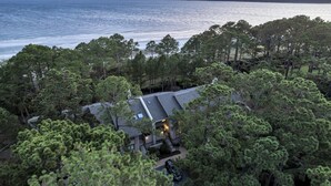 A coastal house surrounded by dense pine trees, with a view of the sea and a boat in the distance.