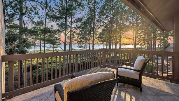 A balcony with wicker furniture and a view of trees and a sunset.