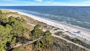 A beach with a clear view of the ocean, a sandy path, and a few trees.