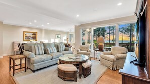 A spacious living room with a large sofa, a glass coffee table, and a television.
