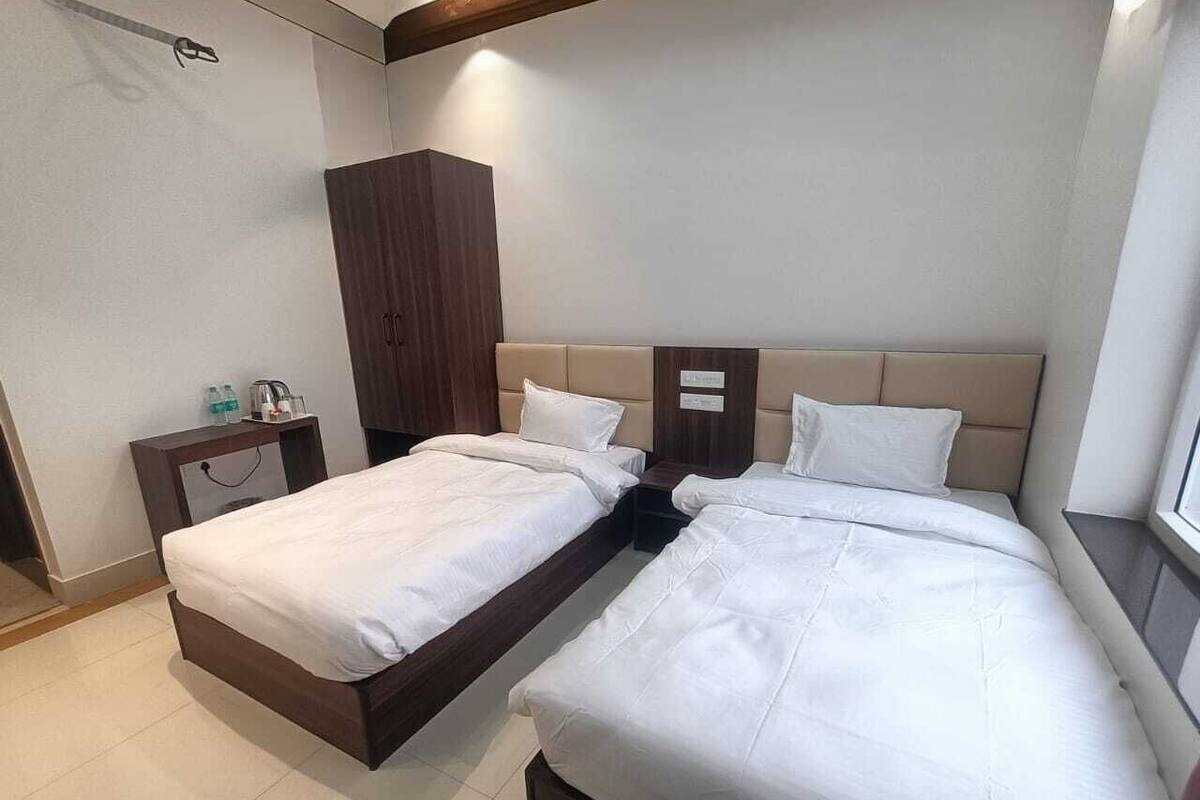 Une chambre d’hôtel avec deux lits simples, une armoire en bois, une table de chevet avec une lampe et une fenêtre donnant sur un beau paysage.