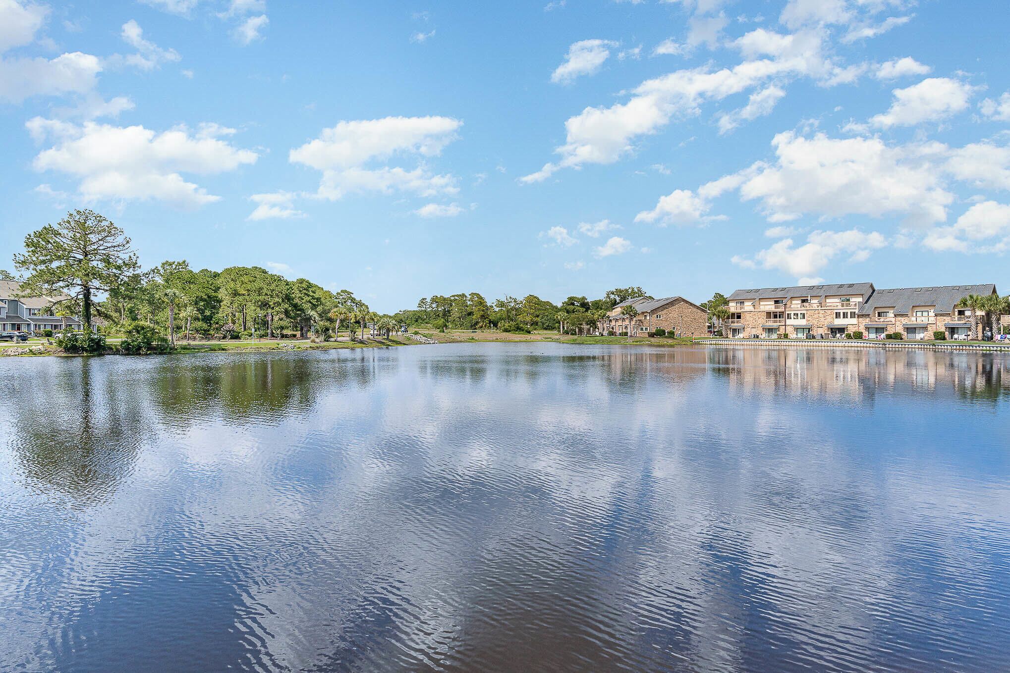 A tranquil lake with a reflection of buildings and trees, surrounded by a well-maintained park and residential buildings.