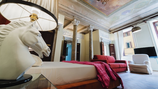 A hotel room with a bed, a red sofa, a white armchair, a ceiling with a fresco, and a large window. - Residenza la Scala (Florence)
