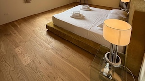 A bedroom with a wooden floor, a bed with white linens, a bedside lamp, a chair, a radiator, and a window with curtains. - Residenza la Scala (Florence)