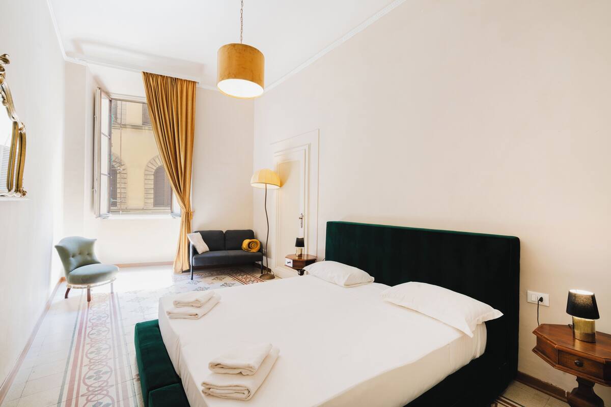 A hotel room with a large bed, a chair, a desk, and a window with curtains.