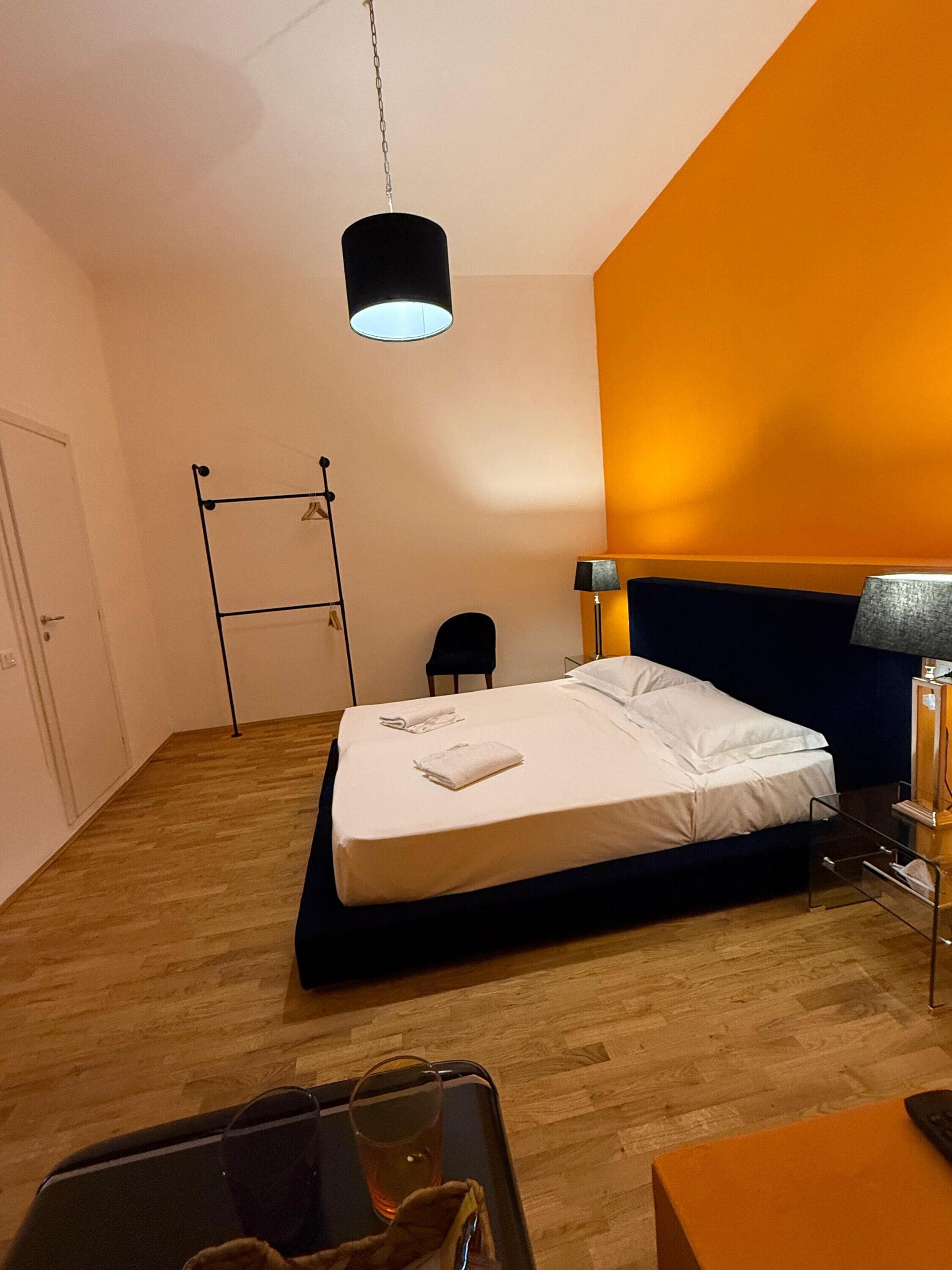 Een hotelkamer met een bed, een bureau, een stoel, een klein tafeltje, een lamp en een hanglamp.