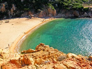 Een kuststrand met helder turquoise water, rotskliffen en een zandstrand.