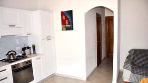 A kitchen with white cabinets, a stove, and an oven. There is a painting on the wall and a door leading to another room.