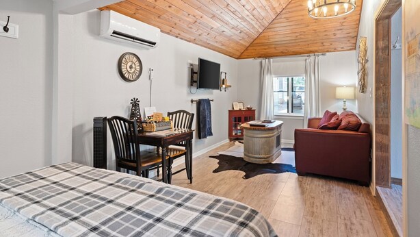 A cozy room with a wooden ceiling, a bed, a dining table with chairs, a red sofa, and a television on the wall. - Private Hot Tub - 1.4 miles to Main Street - 5 minute drive. (Fredericksburg)