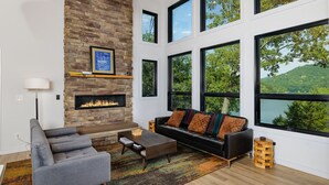 Una sala moderna con chimenea de piedra, ventanas grandes y vista a un lago.