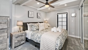 Une chambre à coucher avec un lit, des tables de chevet, un ventilateur de plafond et des œuvres d’art accrochées aux murs.