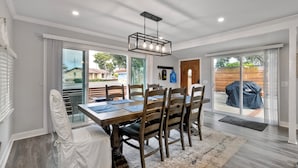 Un espace repas comprenant une table et des chaises en bois, un lustre et de grandes portes-fenêtres coulissantes donnant sur un patio extérieur.