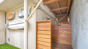 Un escalier en bois mène à un espace abrité où des planches de surf sont fixées au mur.