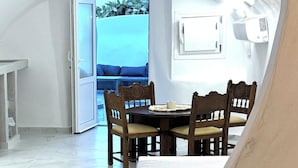 Une vue intérieure d’une pièce comprenant une table à manger et des chaises, un plafond blanc et une vue sur la mer par une porte ouverte.