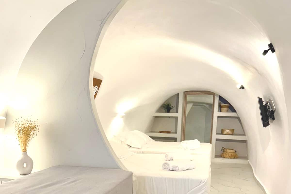 A compact, arched bedroom with a bed, a small bedside table, a decorative rug, and a shelf with items.