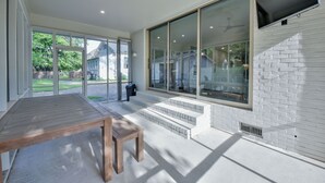 Un patio exterior moderno con una mesa y banco de madera, grandes puertas correderas de vidrio y un televisor montado en la pared.